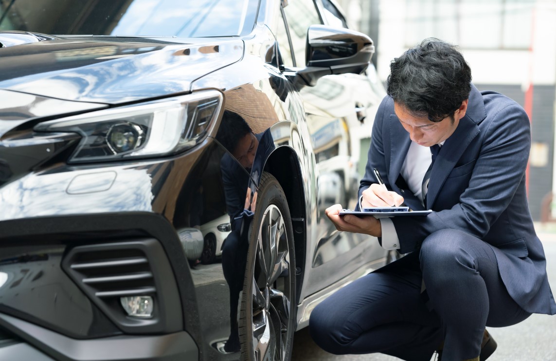 黒い車の側面を査定するビジネスマン