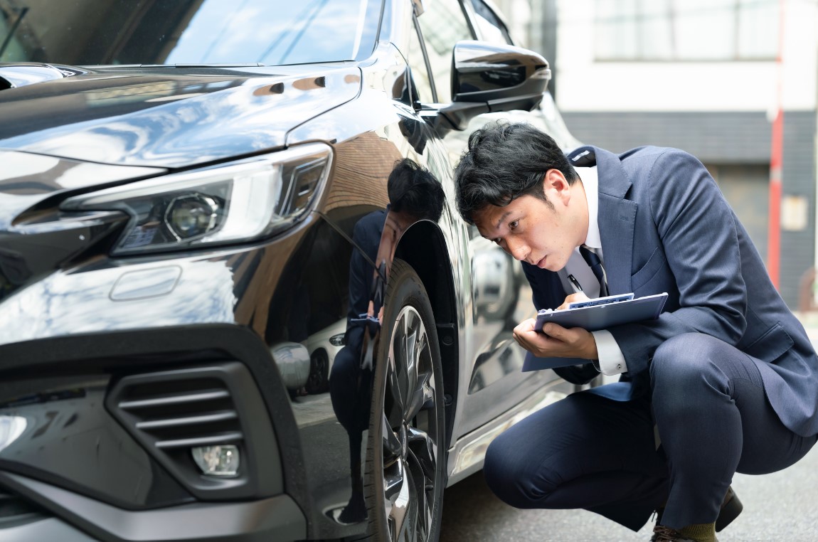 車のタイヤ部分を査定するビジネスマン