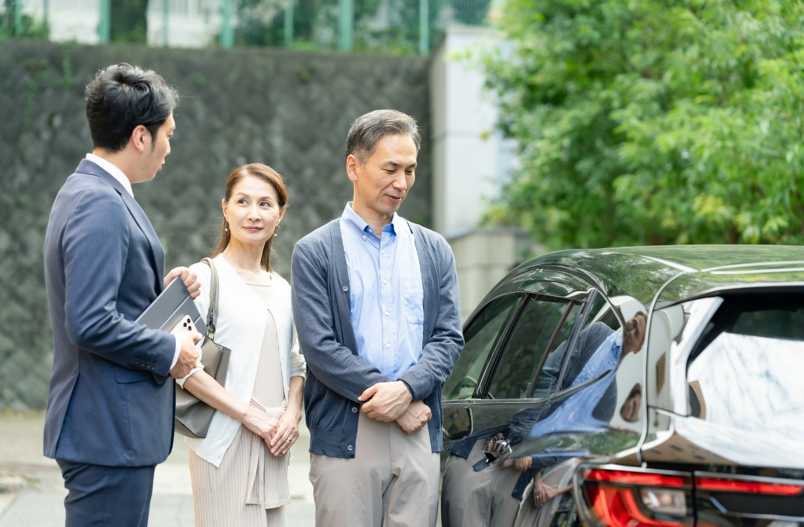 車の横で夫婦に説明をする男性ビジネスマン